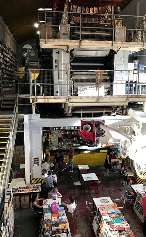 本屋Ler Devagarのカフェスペースと大きな印刷機の画像